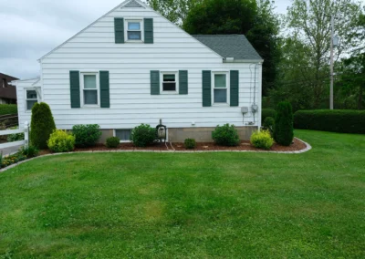 shrubs and plants trimmed in a mulch bed by a home and a lawn