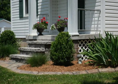 bushes and plants trimmed in a mulch bed by a lawn and porch